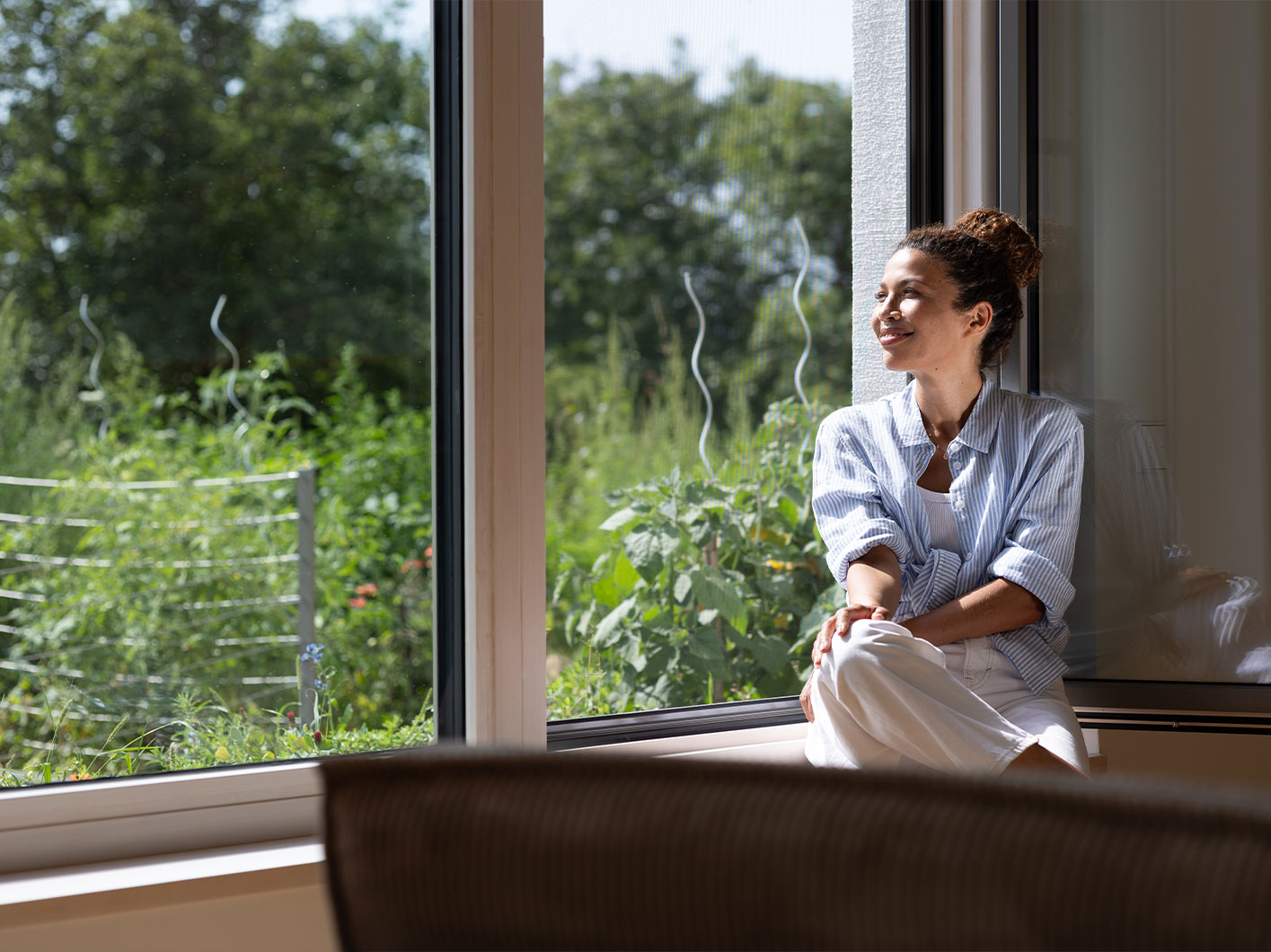 Eine Frau sitzt in einer Wohnung mit offenem Fenster mit Insektenschutz.
